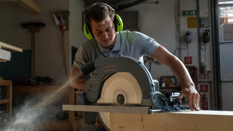 Zimmerer beim Zuschnitt mit der Handkreissäge in der Werkstatt